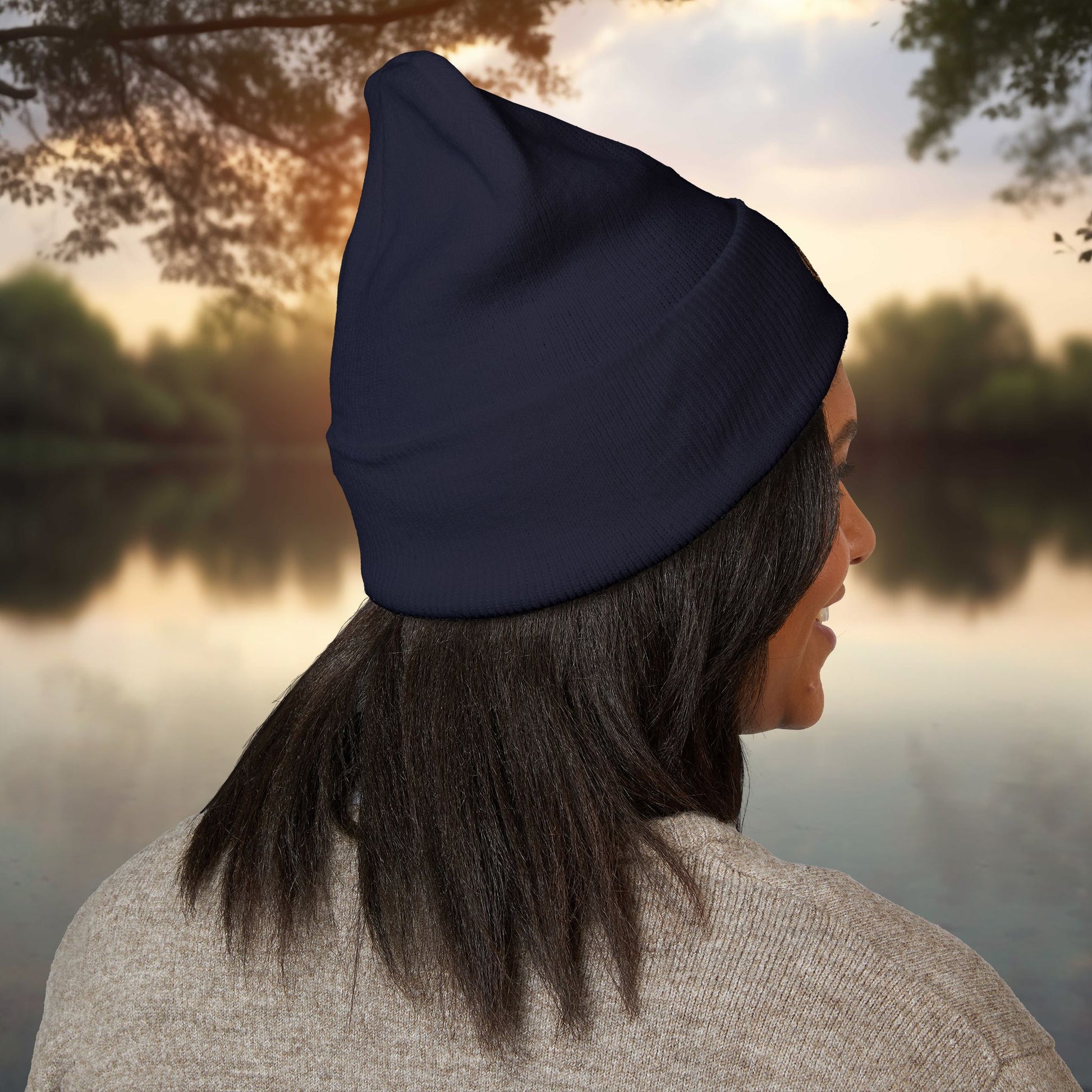 Person wearing a navy EssenceInnoCreate beanie with a scenic background of a lake and trees.