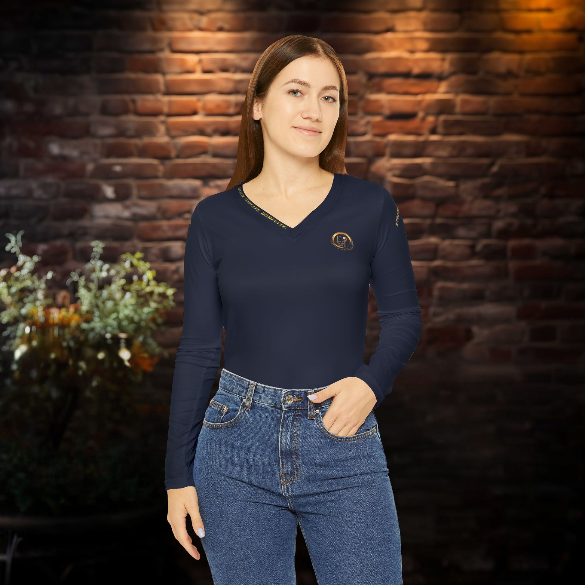 Woman wearing a navy blue long-sleeve Essence Innovation top and jeans against a brick wall.