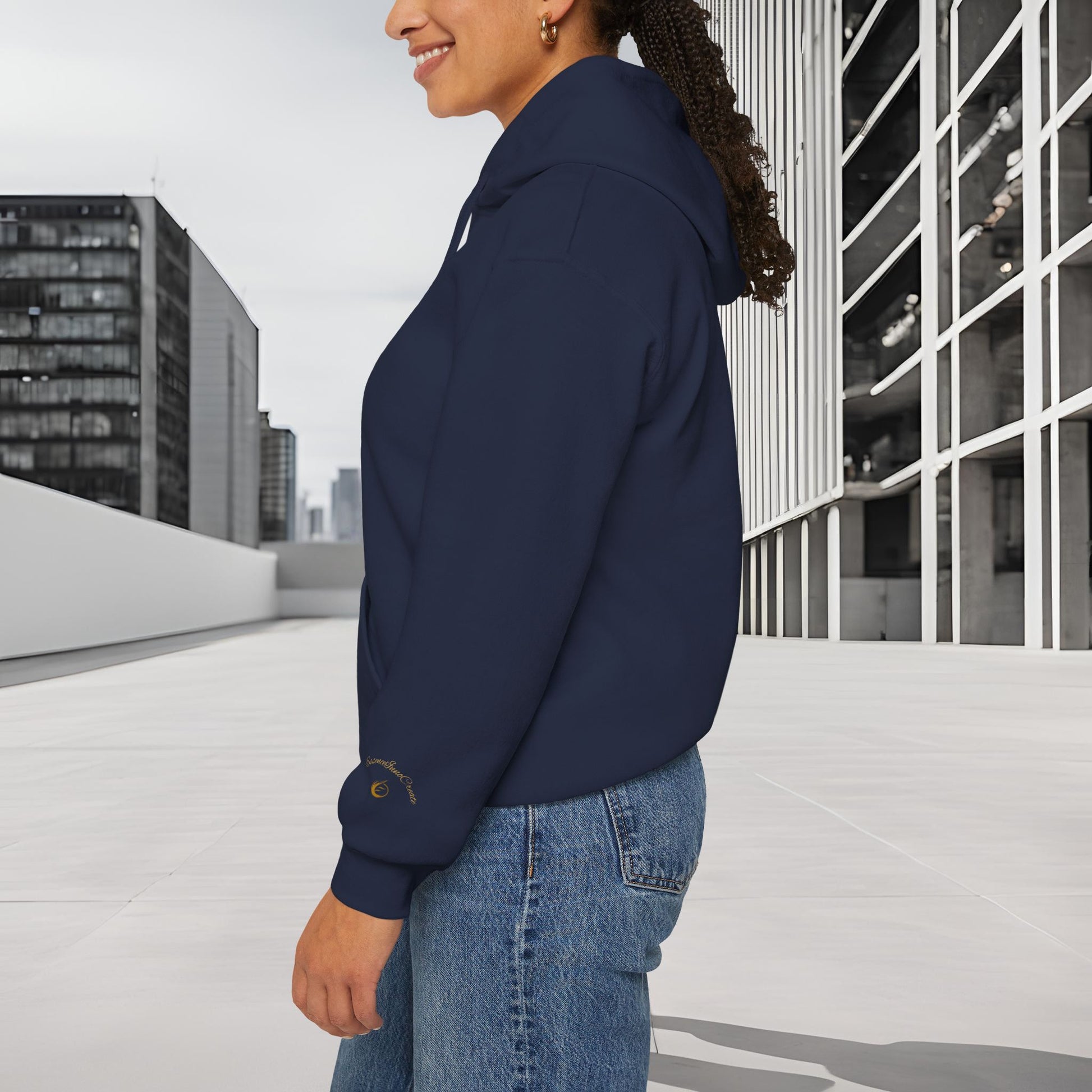 Person wearing a navy blue 'EssenceInnoCreate' hoodie and jeans standing in an urban setting with modern buildings.