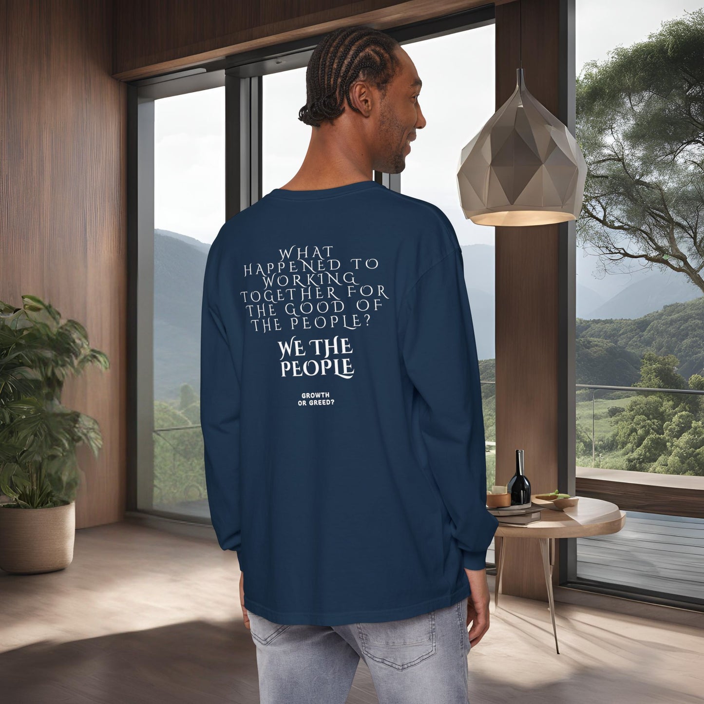Man wearing a blue long-sleeve EssenceInnoCreate Quiet Resolve shirt with text in a modern room with large windows.
