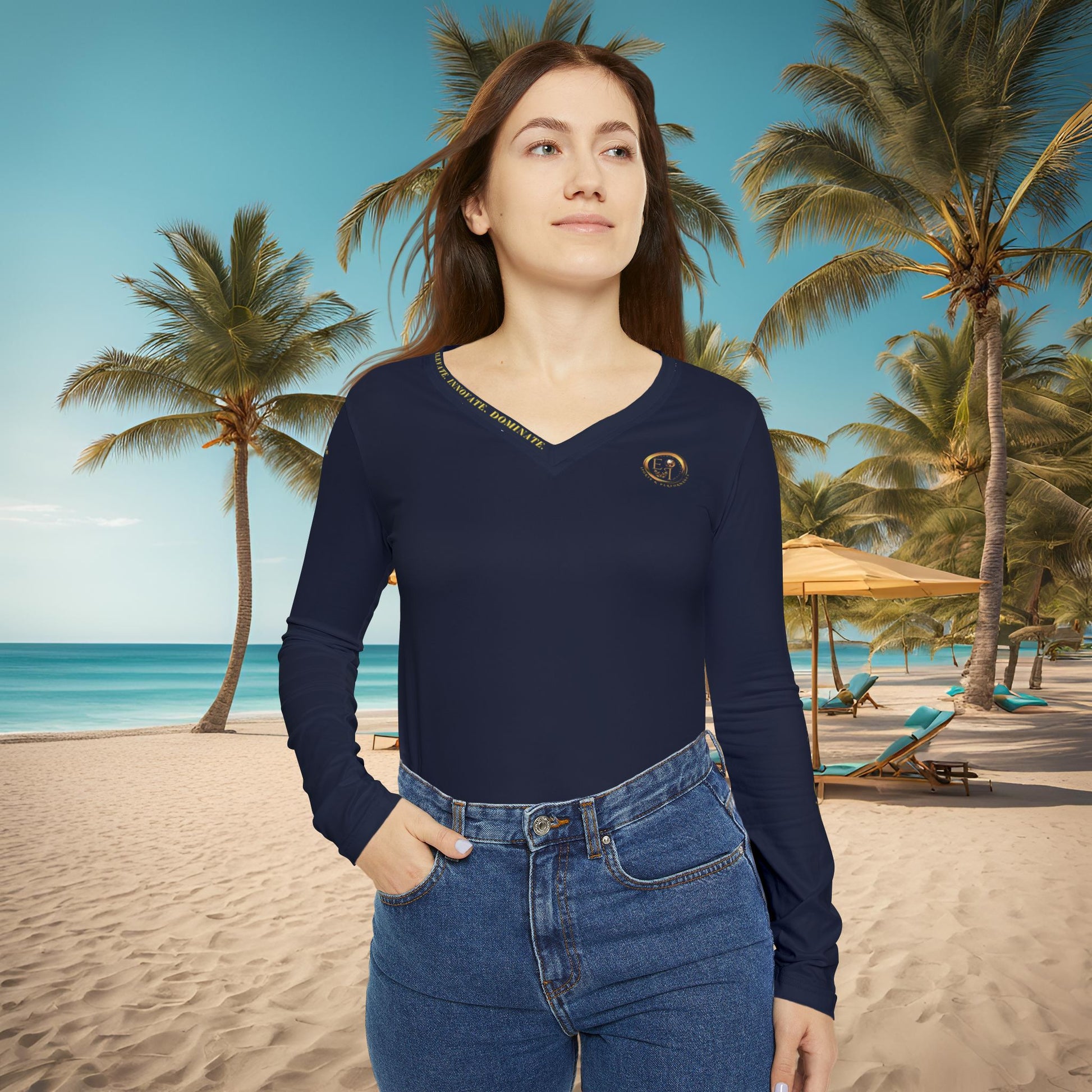 Woman wearing a navy blue long-sleeve Essence Innovation top and jeans on a beach with palm trees and ocean in the background.