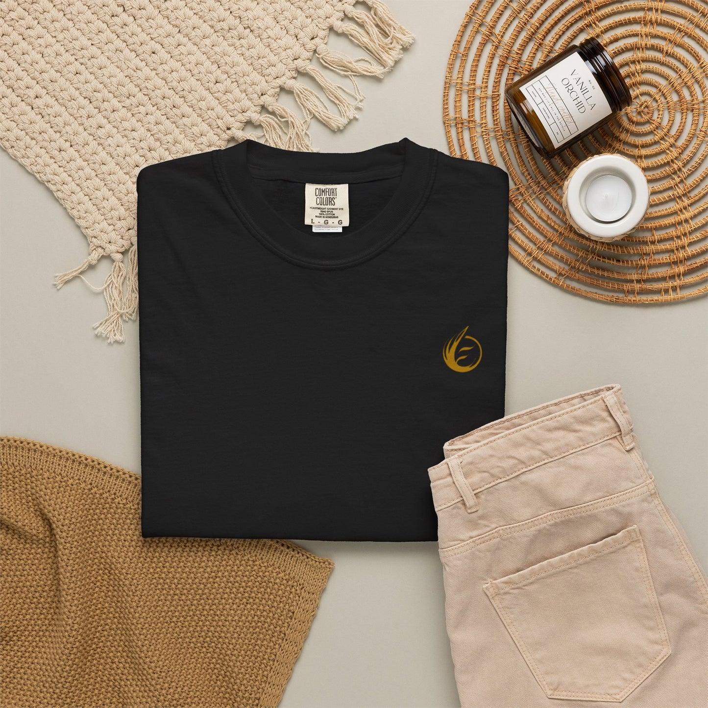 Black t-shirt with a gold 'EssenceInnoCreate' logo on a neutral surface with beige pants and decorative items.