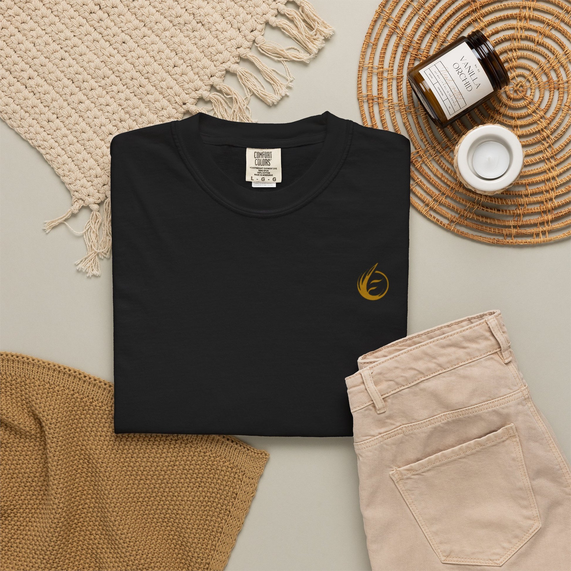 Black t-shirt with a gold 'EssenceInnoCreate' logo on a neutral surface with beige pants and decorative items.
