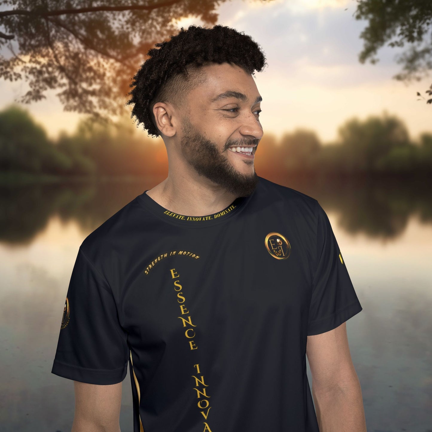 Man wearing a black t-shirt with gold Essence Innovation logo and text and design, standing outdoors with a blurred natural background