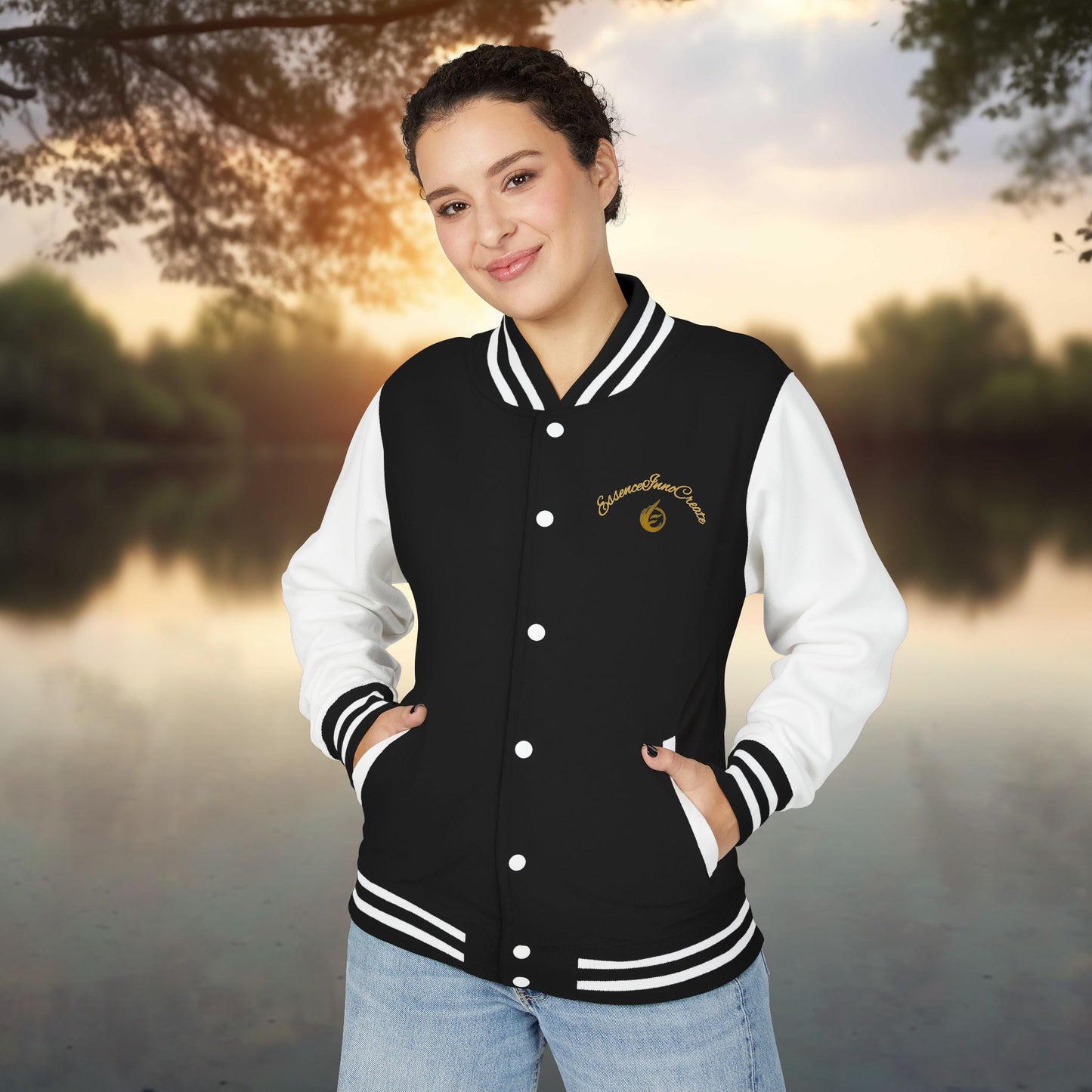 Person wearing a black and white varsity jacket with a EssenceInnoCreate logo, standing outdoors with a scenic background.