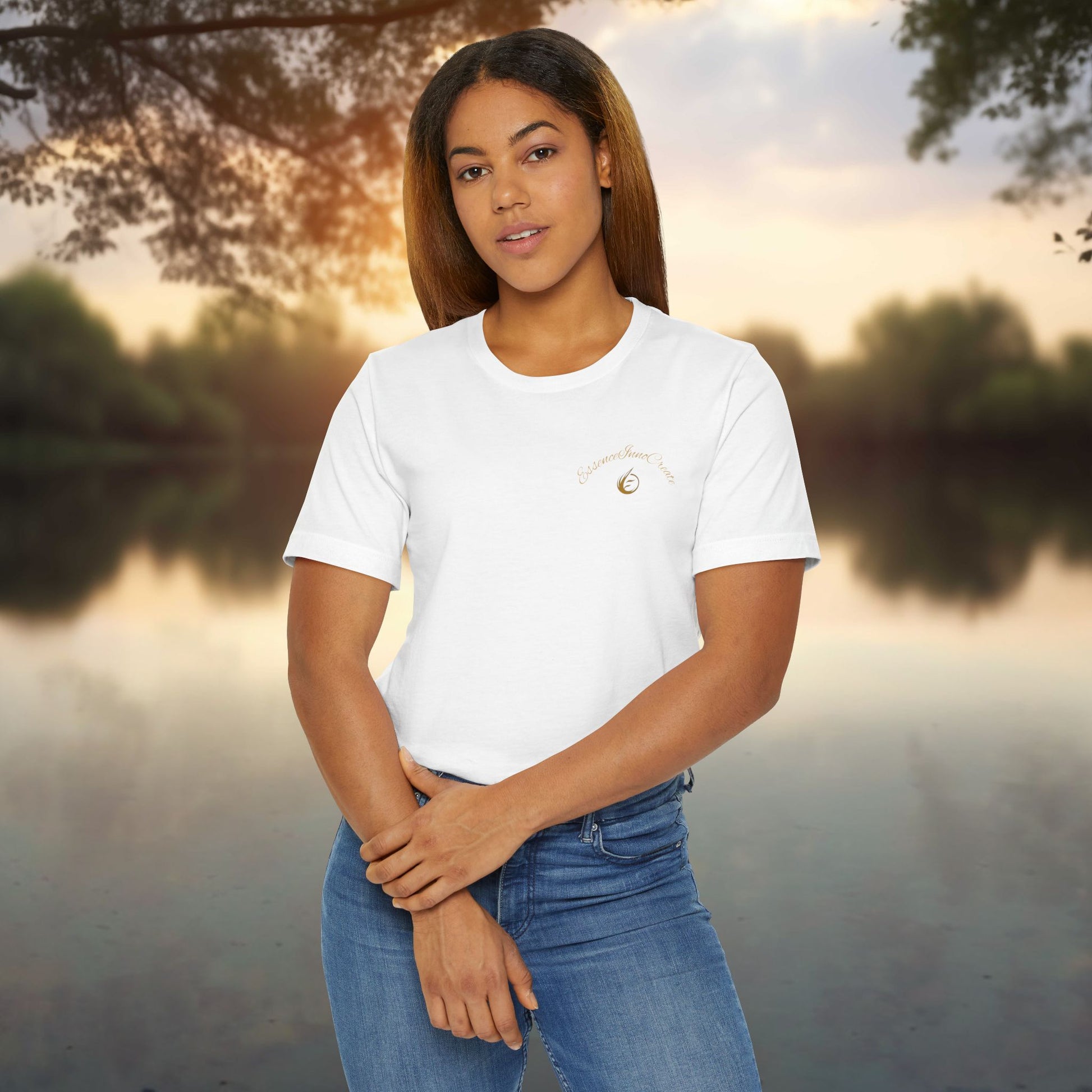 Woman wearing a white t-shirt with 'EssenceInnoCreate' logo standing by a lake at sunset.