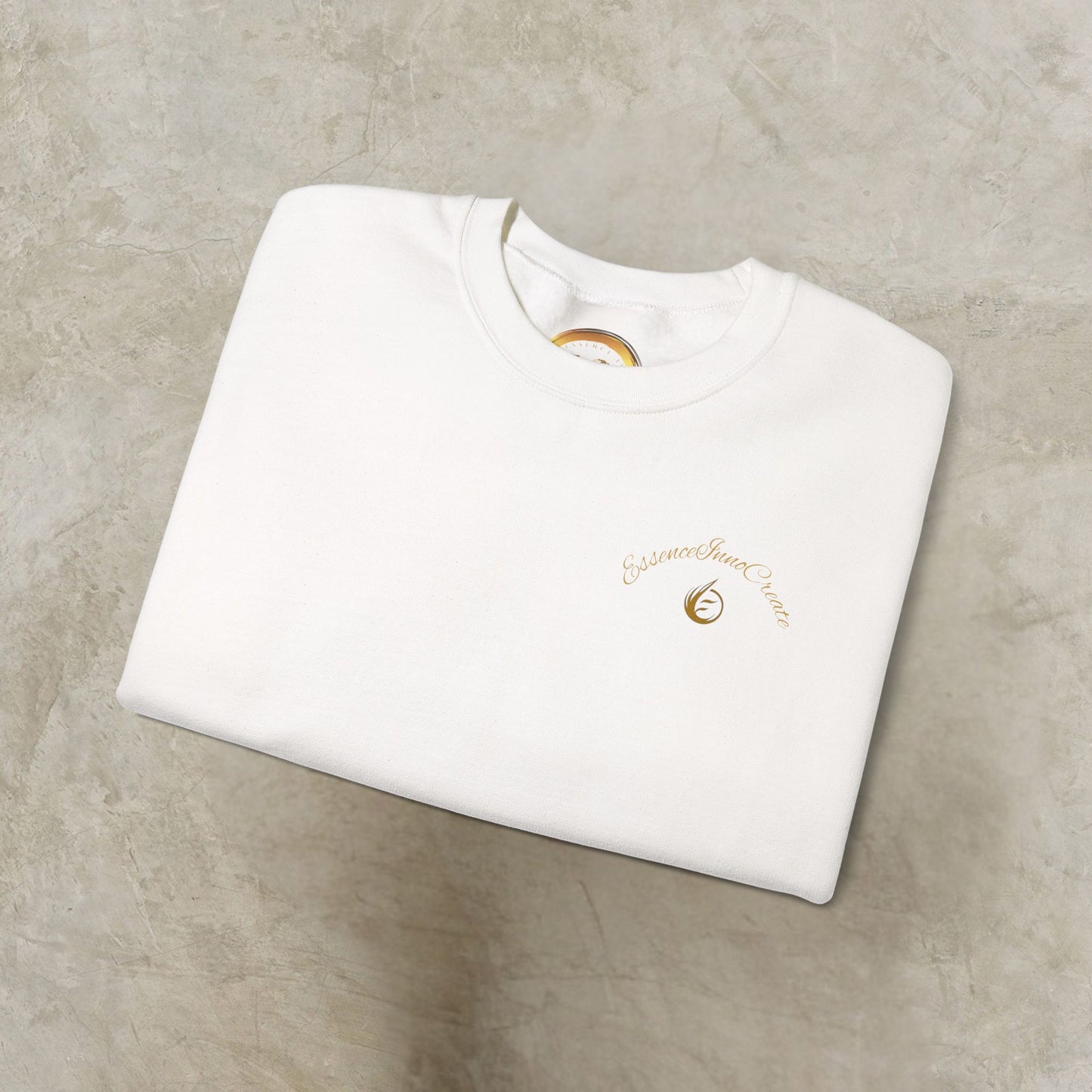White sweatshirt with gold 'EssenceInnoCreate' embroidery on a beige surface