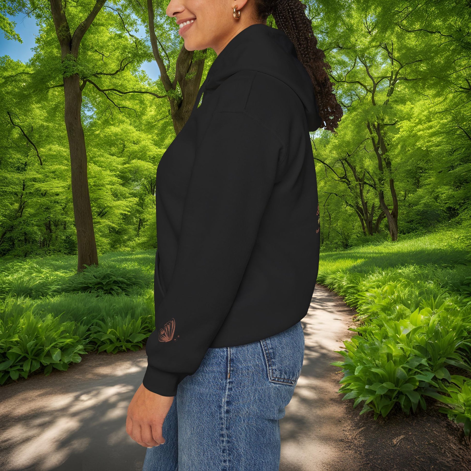 Person wearing a black Essence Innovation Bohemian Butterfly Crest hoodie with a logo in a park setting