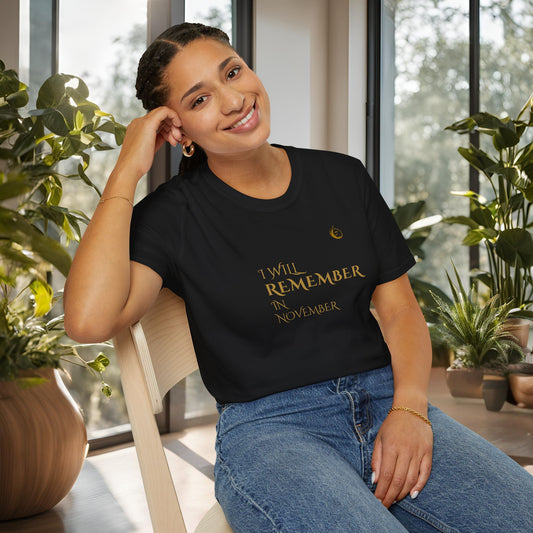 Woman wearing a black EssenceInnoCreate Quiet Resolve t-shirt with text, sitting indoors with plants around.