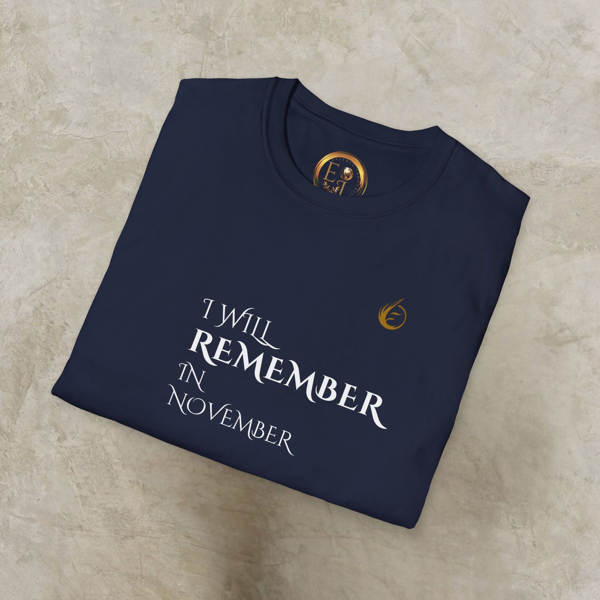 Folded navy blue EssenceInnoCreate Quiet Resolve sweatshirt with text 'I Will Remember In November' on a beige surface