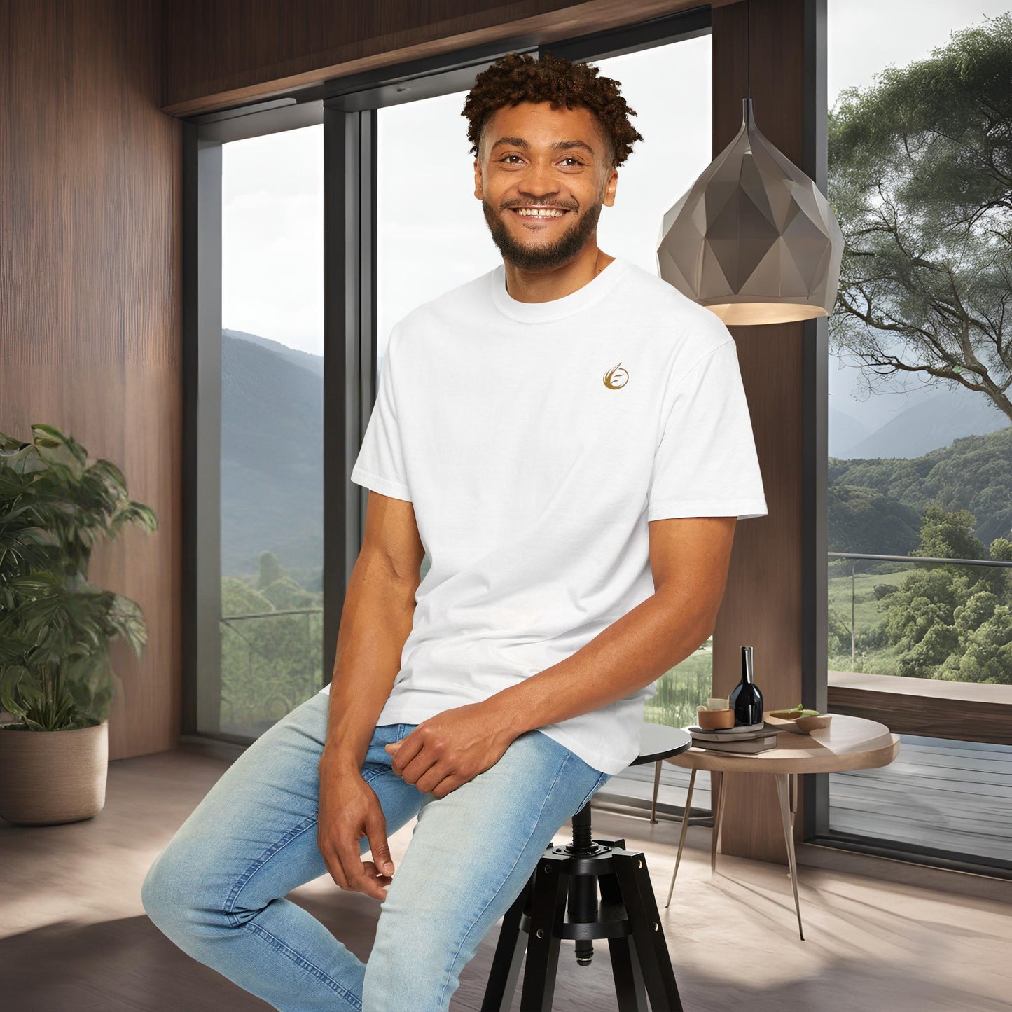 Man sitting on a stool in a modern room with large windows and a scenic view in a 'EssenceInnoCreate' T-shirt.