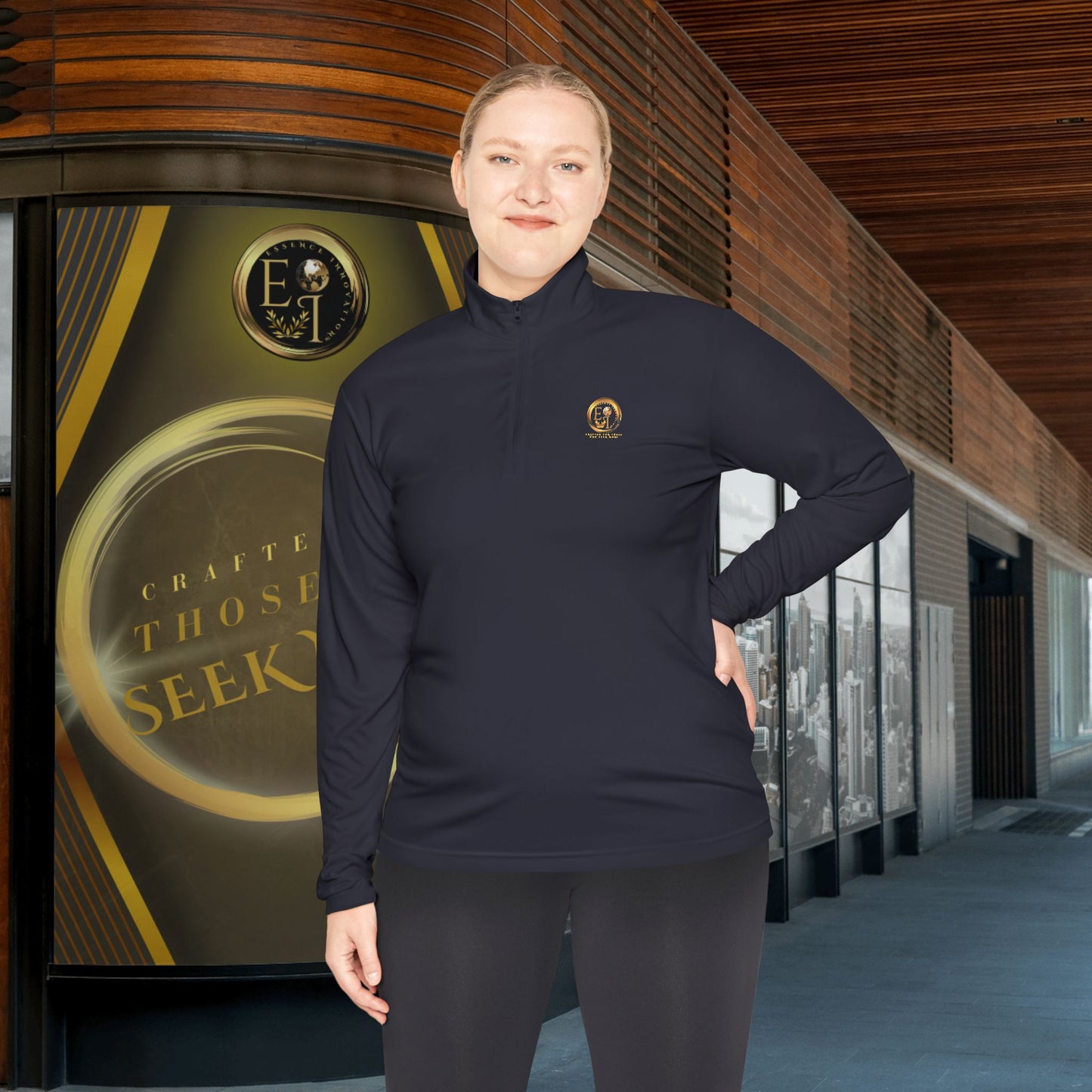 Person wearing a dark blue Essence Innovation Seek More pullover with a logo, standing in front of a building entrance.