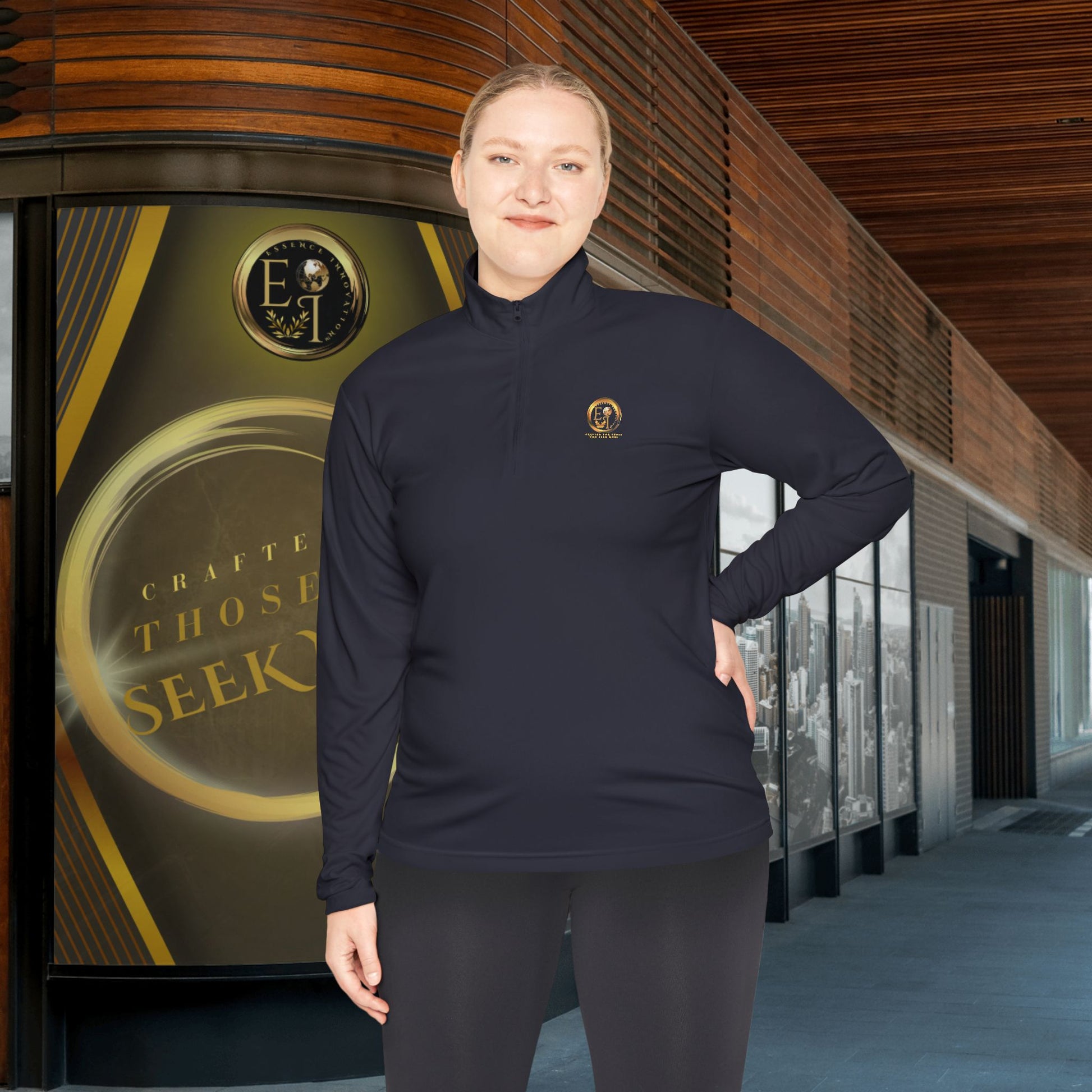 Person wearing a dark blue Essence Innovation Seek More pullover with a logo, standing in front of a building entrance.