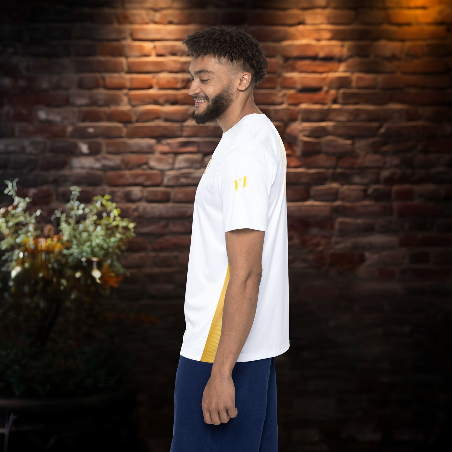 Man wearing a white t-shirt with a yellow logo against a brick wall.