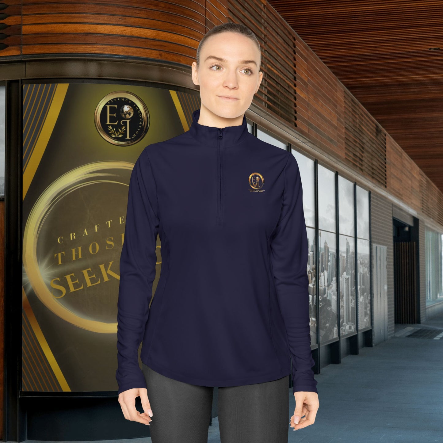 Person wearing a navy blue Essence Innovation Seek More quarter-zip long-sleeve shirt with a logo in front of a building with a sign.