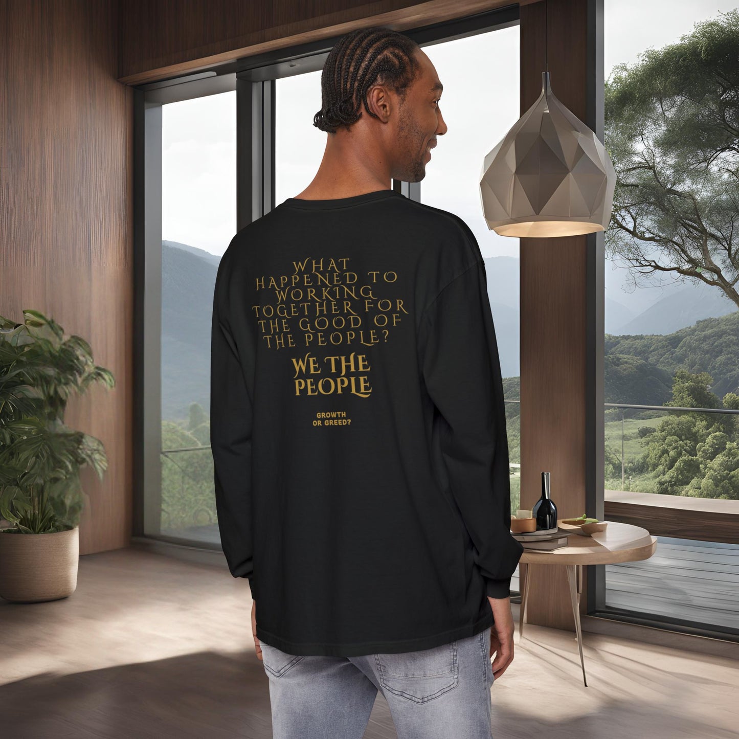 Man wearing a black long-sleeve EssenceInnoCreate Quiet Resolve shirt with text in a modern room with large windows.