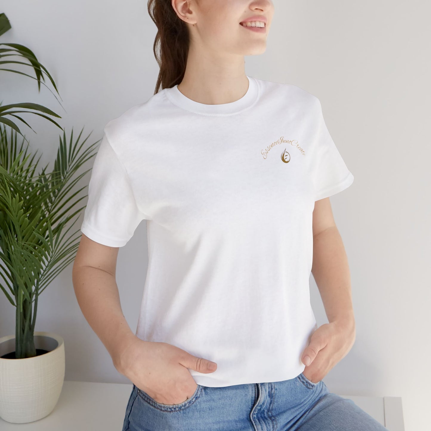Person wearing a white t-shirt with a small 'EssenceInnoCreate' design, standing indoors next to a plant.