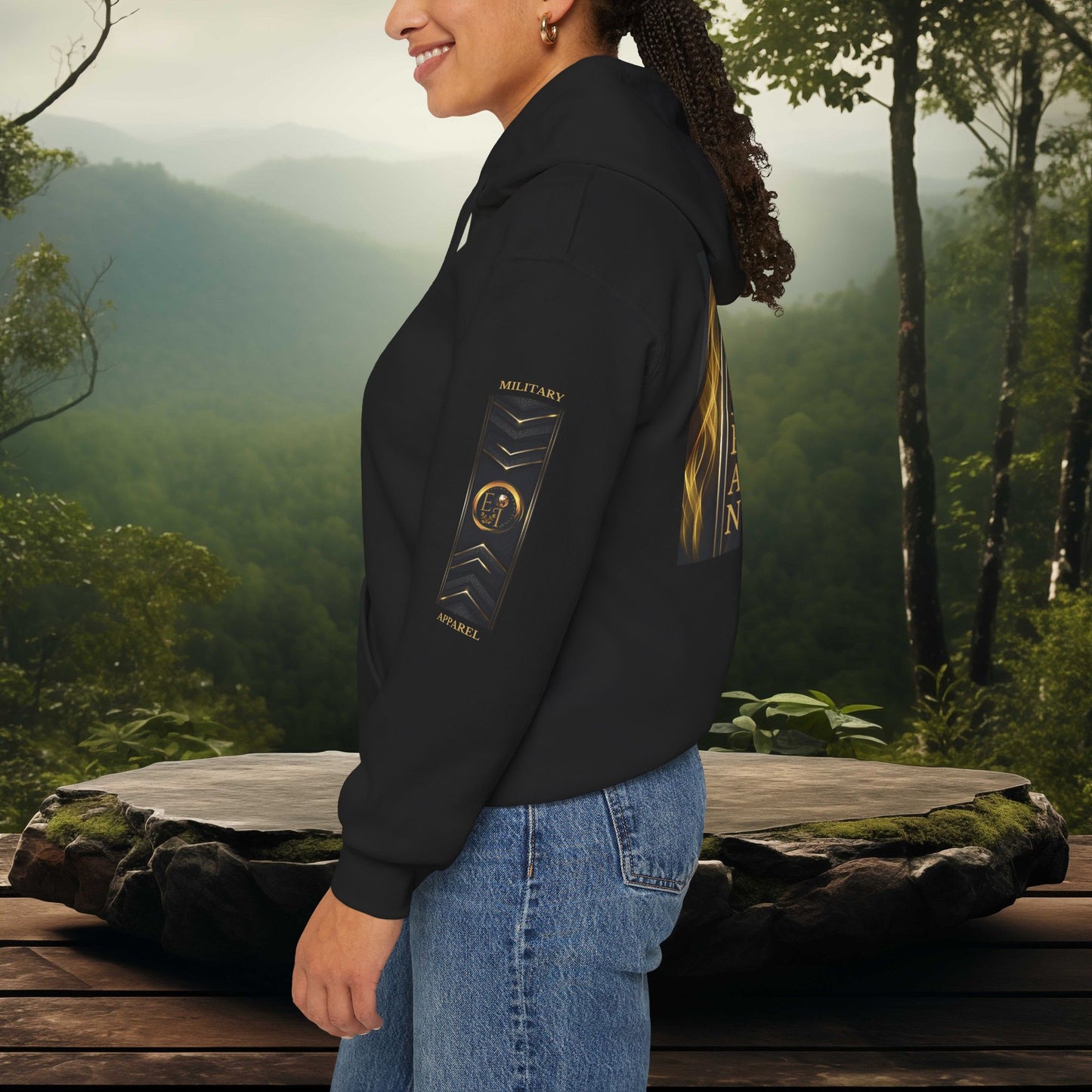 Person wearing a black Essence Innovation hoodie with a military apparel design in a forest setting