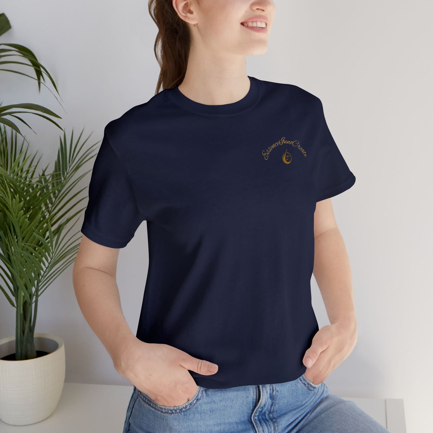 Person wearing a navy blue t-shirt with 'EssenceInnoCreate' logo, standing indoors next to a plant.