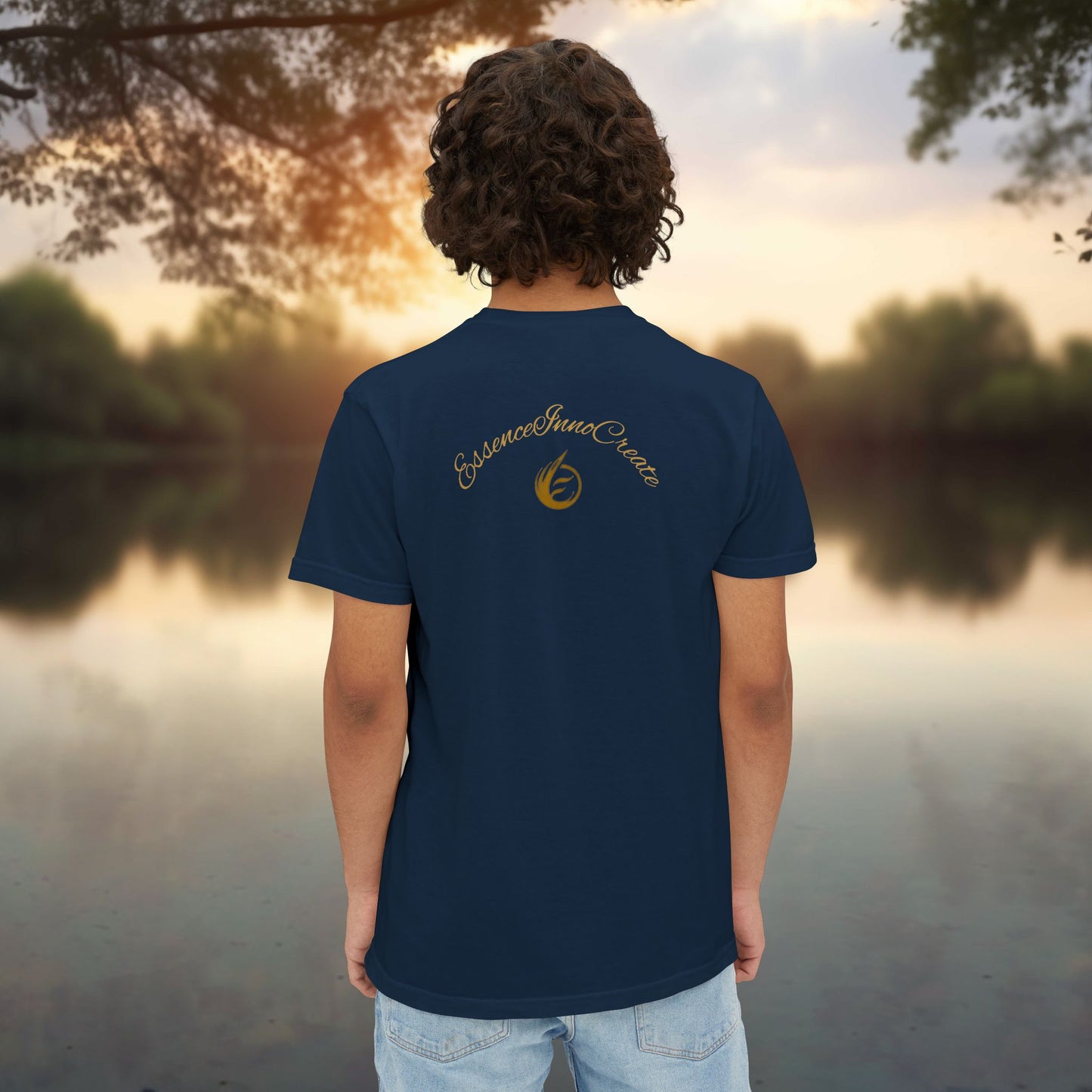 Person wearing a blue t-shirt with 'EssenceInnoCreate' logo, standing by a lake at sunset.