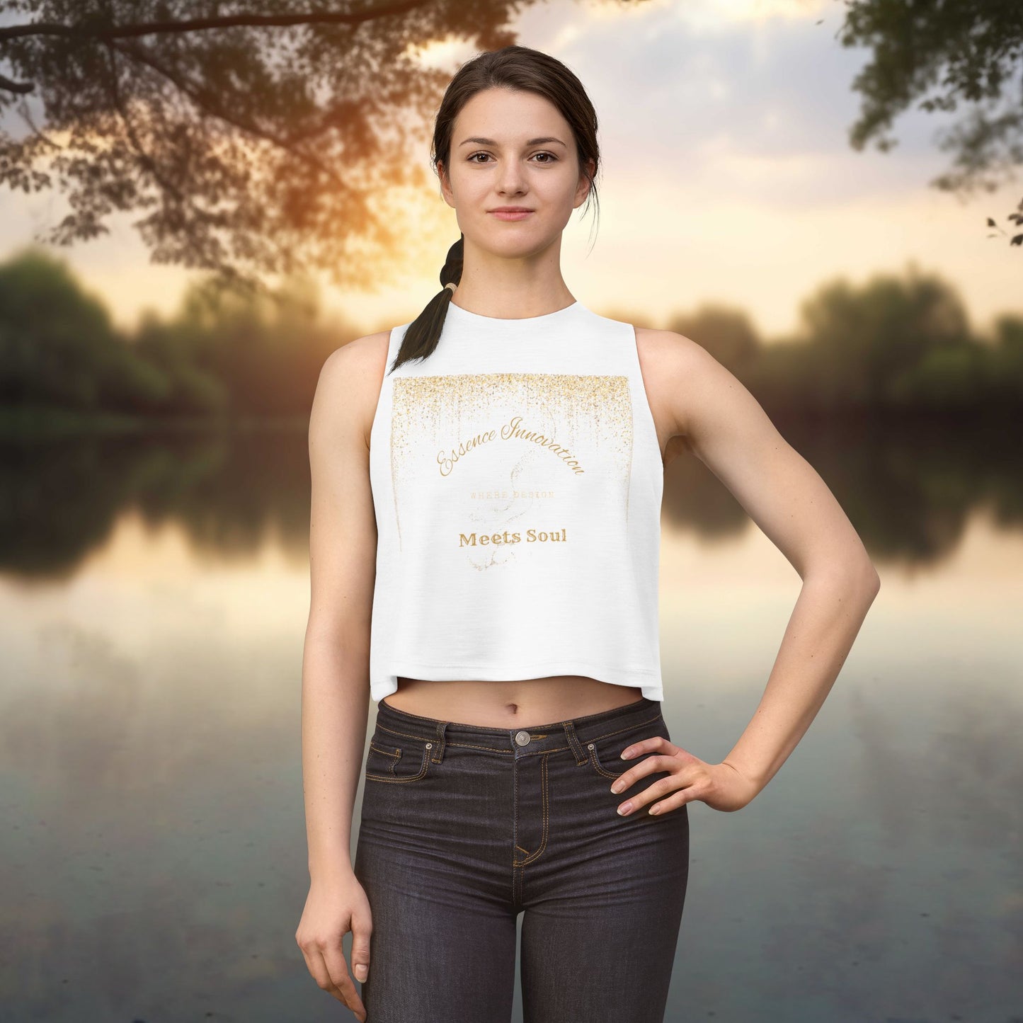 Woman wearing a white Essence Innovation 'Design Meets Soul' sleeveless top with text standing by a lake at sunset.