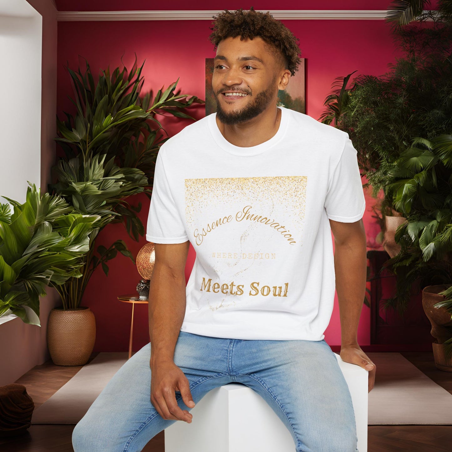 Man sitting on a white stool wearing a white Essence Innovation 'Design Meets Soul' t-shirt in a room with plants and a red wall.