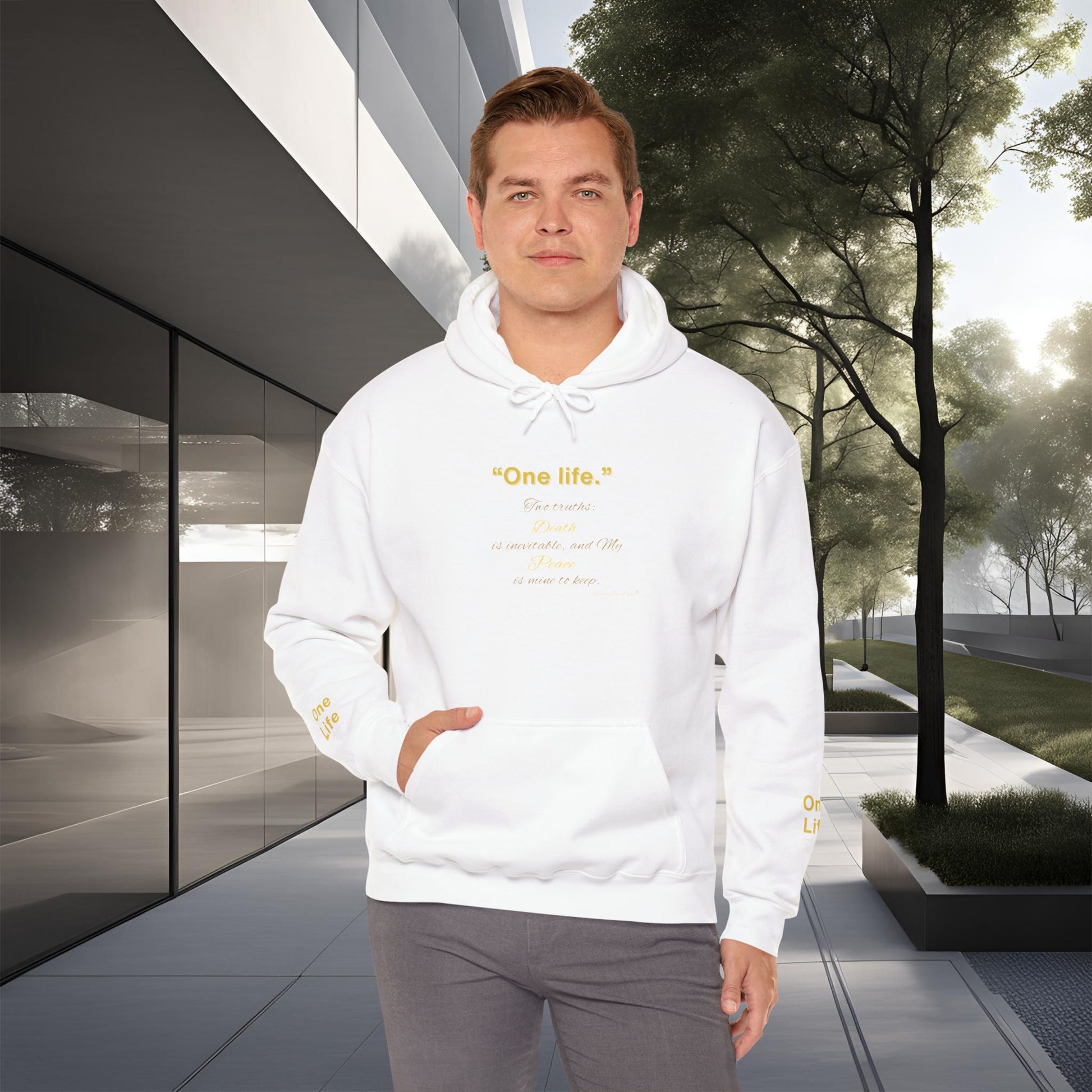 Man wearing a white Essence Innovation 'One Life' hoodie with text standing in front of modern architecture and trees.