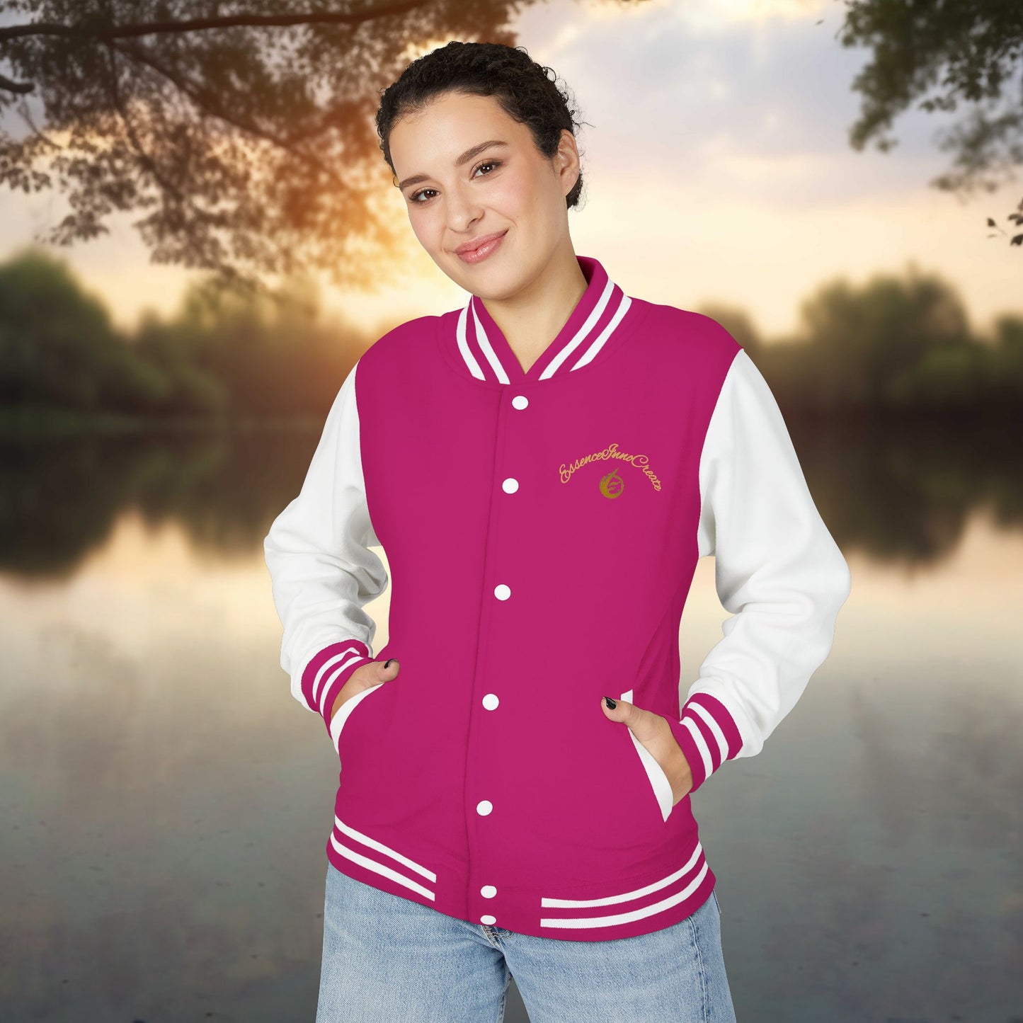 Person wearing a pink and white varsity jacket with a EssenceInnoCreate logo, standing outdoors with a blurred natural background.
