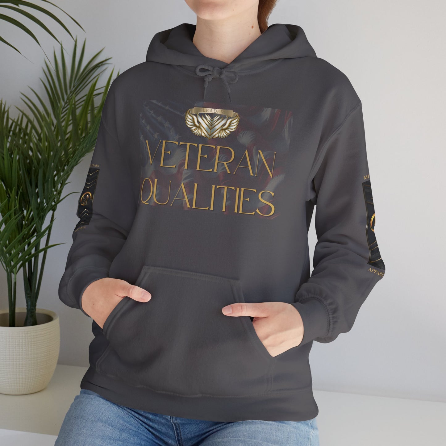 Person wearing a dark gray Essence Innovation hoodie with 'Veteran Qualities' text and logo, standing indoors next to a plant.