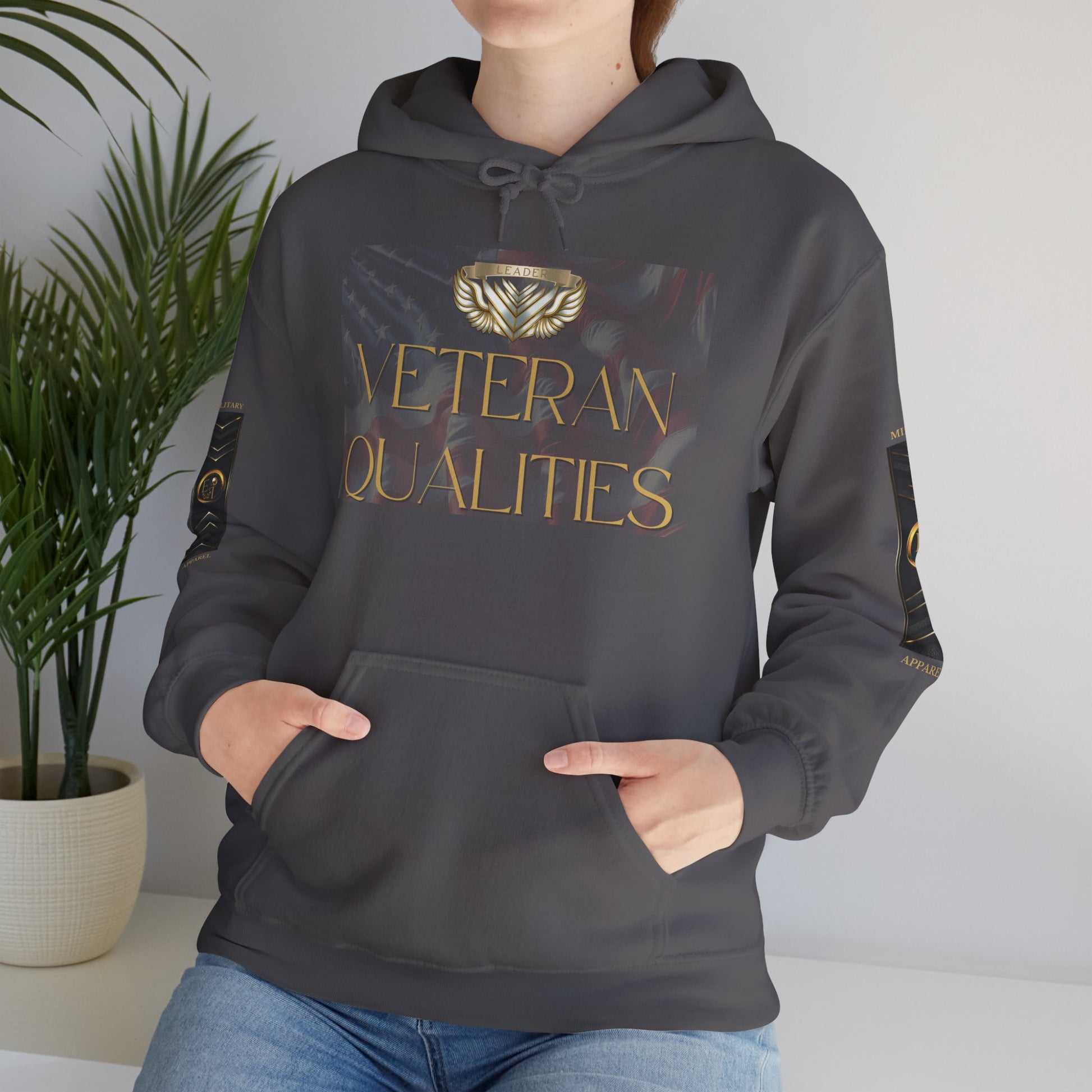 Person wearing a dark gray Essence Innovation hoodie with 'Veteran Qualities' text and logo, standing indoors next to a plant.